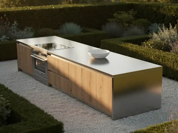 Strakke buitenkeuken met geborsteld staal en warm eikenhout, omgeven door strakgesnoeid groen en licht grind in zacht middaglicht.