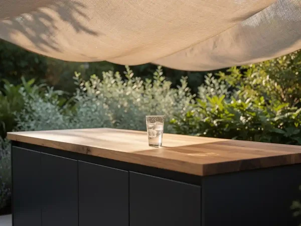 Buitenkeuken van staal en eikenhout op beschaduwd terras, met condensglas op het werkblad en weelderig groen op de achtergrond.